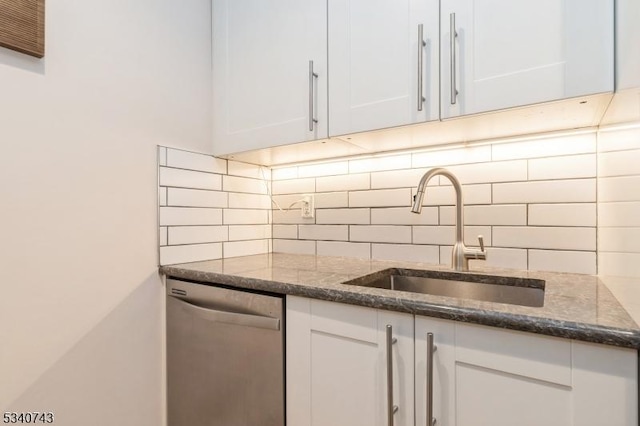 kitchen featuring decorative backsplash, dark stone counters, stainless steel dishwasher, white cabinetry, and a sink