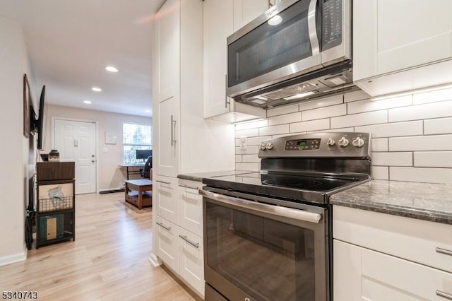 kitchen with stainless steel appliances, white cabinets, light wood finished floors, tasteful backsplash, and dark stone countertops