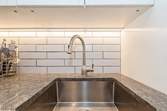 interior details with tasteful backsplash, a sink, and dark stone countertops