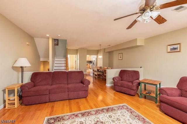 living room featuring ceiling fan, wood finished floors, visible vents, baseboards, and stairs