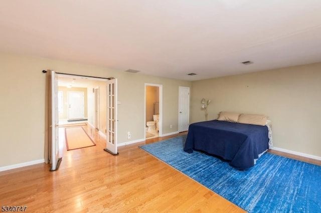 bedroom featuring ensuite bath, light wood-style flooring, visible vents, and baseboards