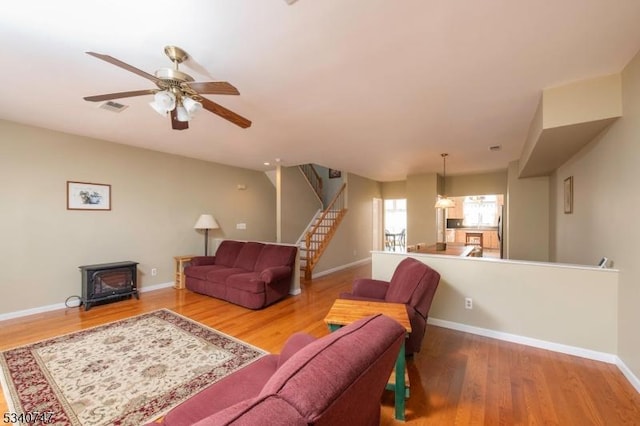 living area featuring visible vents, a wood stove, wood finished floors, baseboards, and stairs