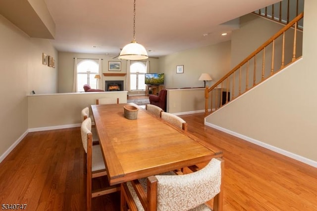 dining room featuring a warm lit fireplace, stairway, baseboards, and wood finished floors