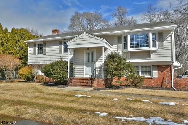 split foyer home featuring brick siding, a chimney, and a front yard