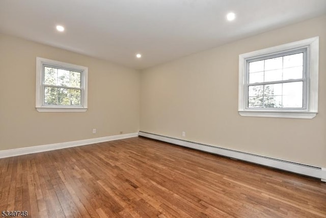 unfurnished room featuring a baseboard heating unit, plenty of natural light, baseboards, and wood finished floors