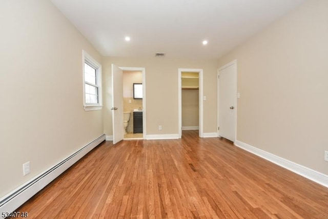 unfurnished bedroom with visible vents, baseboards, light wood-style flooring, a spacious closet, and a baseboard heating unit