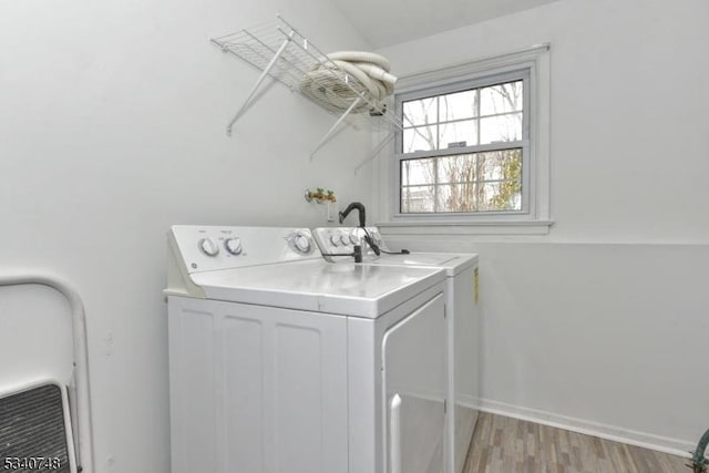 clothes washing area with washing machine and dryer, laundry area, baseboards, and light wood finished floors