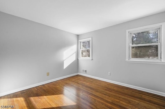 spare room with baseboards, visible vents, and wood finished floors