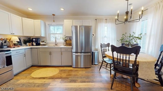 kitchen featuring stainless steel appliances, a sink, hanging light fixtures, light countertops, and light wood finished floors