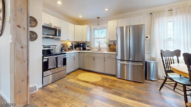 kitchen with a sink, visible vents, ornamental molding, appliances with stainless steel finishes, and light wood-type flooring