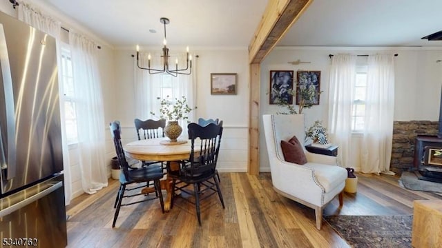 dining area featuring a wood stove, ornamental molding, a chandelier, and wood finished floors