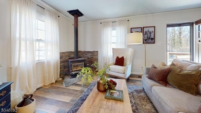 living area with ornamental molding, a wood stove, a healthy amount of sunlight, and wood finished floors