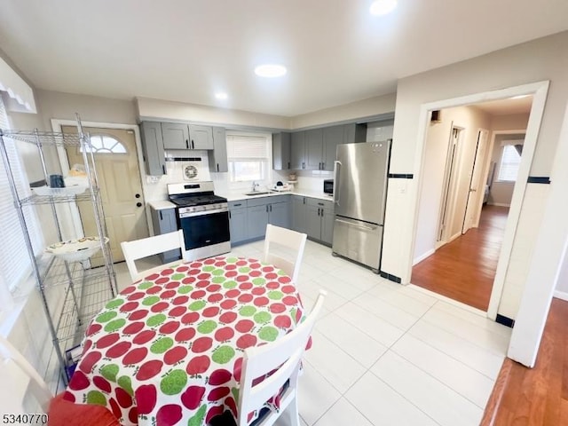 kitchen featuring appliances with stainless steel finishes, light countertops, gray cabinetry, a sink, and light tile patterned flooring