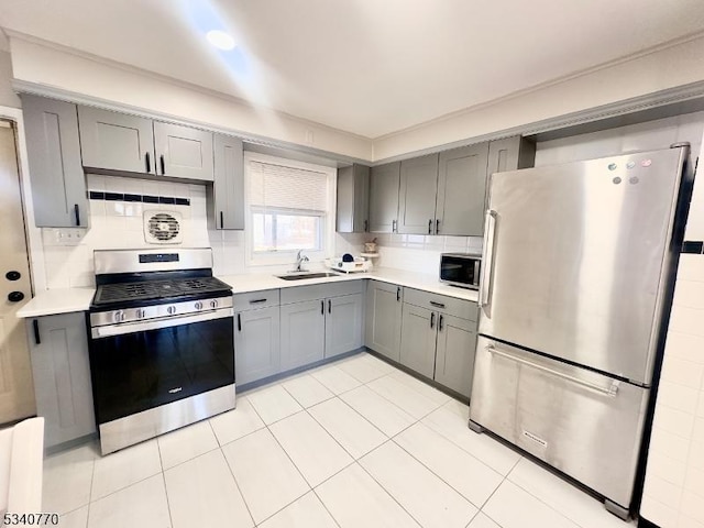 kitchen featuring stainless steel appliances, gray cabinets, light countertops, and a sink