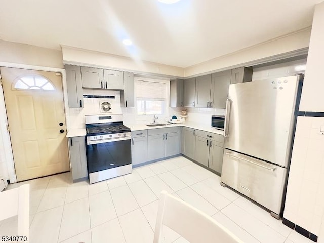 kitchen featuring gray cabinets, light countertops, backsplash, appliances with stainless steel finishes, and a sink