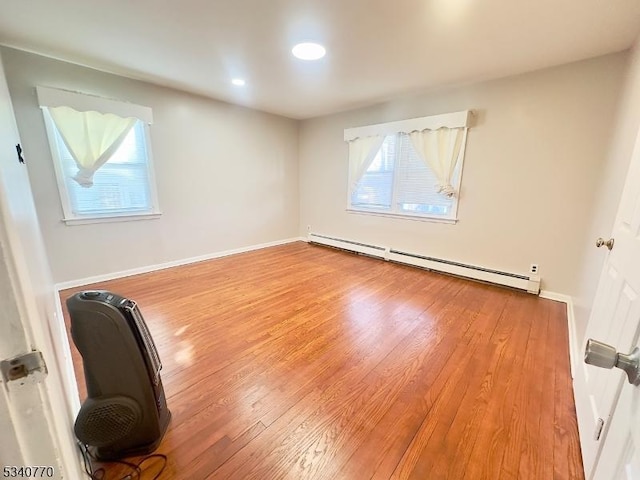 empty room featuring a baseboard radiator, baseboards, and wood finished floors