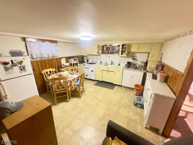 kitchen with white appliances, wooden walls, light countertops, light floors, and a sink