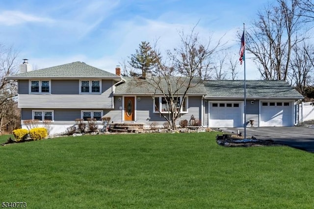 split level home featuring aphalt driveway, a front yard, a chimney, and an attached garage