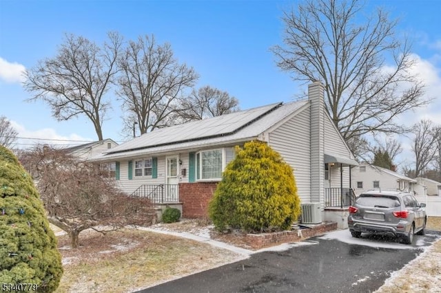 view of front of property featuring brick siding, a chimney, roof mounted solar panels, cooling unit, and driveway