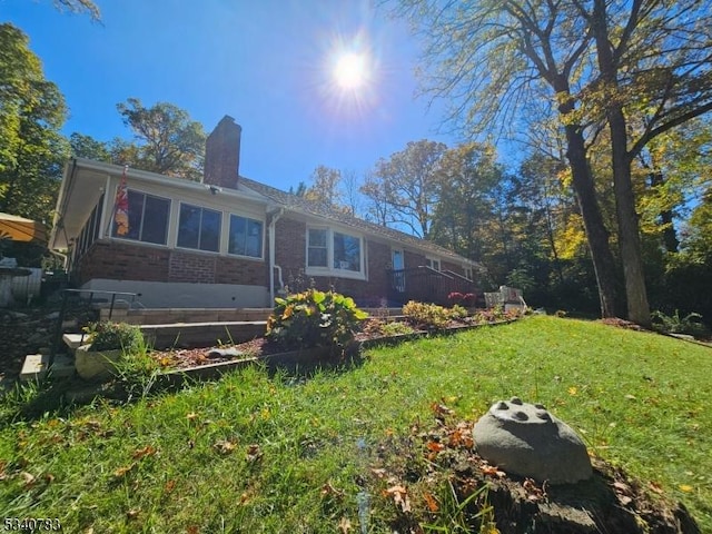 rear view of property featuring brick siding, a chimney, and a lawn