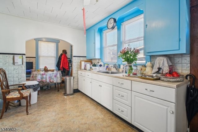 kitchen with a sink, arched walkways, tile walls, and light countertops