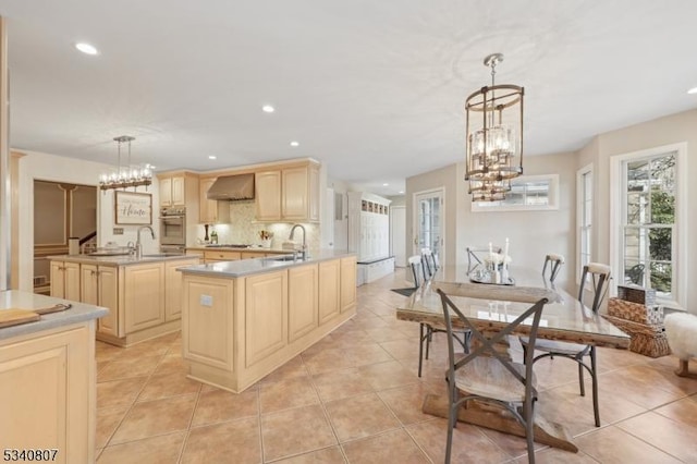 kitchen with oven, a notable chandelier, wall chimney exhaust hood, and light brown cabinetry