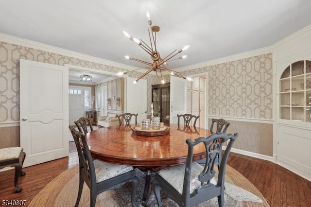 dining area with a wainscoted wall, ornamental molding, wood finished floors, and wallpapered walls