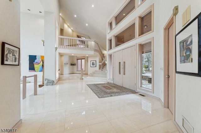 foyer entrance featuring a towering ceiling, marble finish floor, visible vents, and stairway