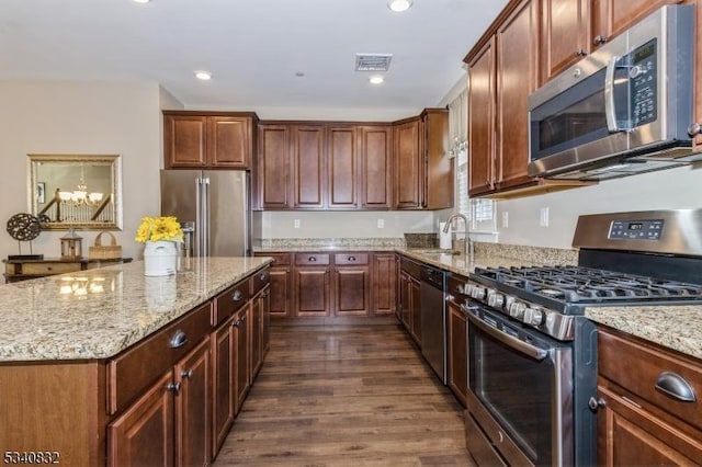 kitchen with stainless steel appliances, visible vents, dark wood-type flooring, a sink, and light stone countertops