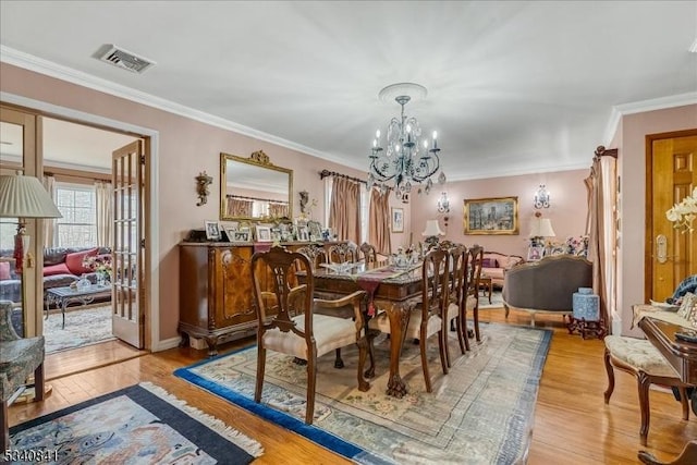 dining space with crown molding, light wood-style flooring, visible vents, and an inviting chandelier