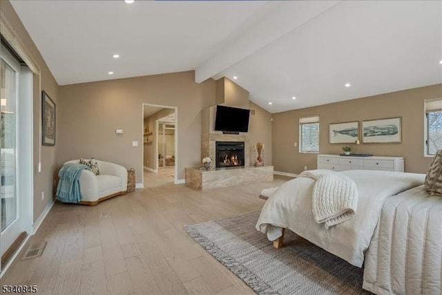 bedroom with light wood finished floors, a fireplace, vaulted ceiling with beams, and baseboards