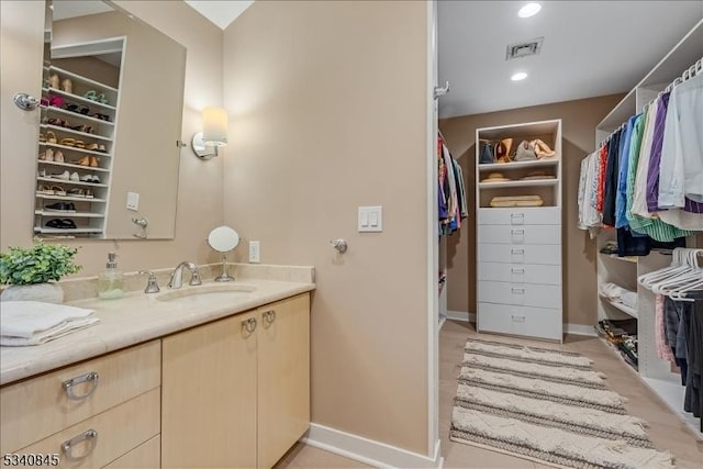 bathroom with a spacious closet, visible vents, baseboards, recessed lighting, and vanity