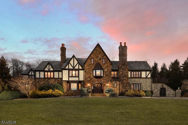 english style home featuring stone siding, a chimney, and a lawn