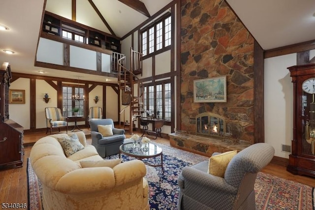 living area featuring a chandelier, vaulted ceiling with beams, a stone fireplace, wood finished floors, and baseboards