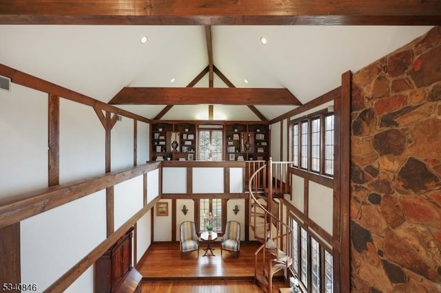 interior space featuring beam ceiling, visible vents, an upstairs landing, wood finished floors, and high vaulted ceiling