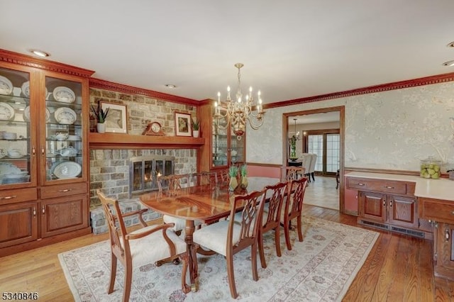 dining room with ornamental molding, a glass covered fireplace, light wood-style flooring, and wallpapered walls