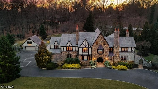 view of front facade featuring a garage, stone siding, a chimney, and an outdoor structure