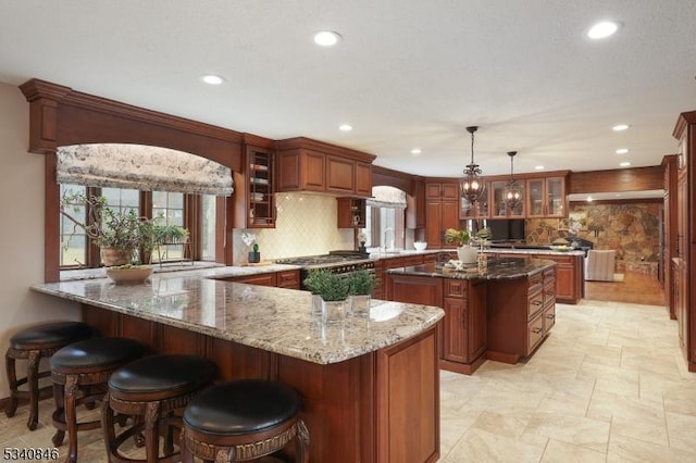 kitchen featuring a peninsula, light stone counters, glass insert cabinets, and decorative backsplash