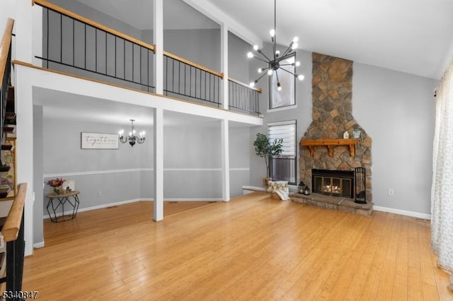 unfurnished living room featuring baseboards, wood finished floors, a stone fireplace, high vaulted ceiling, and a notable chandelier