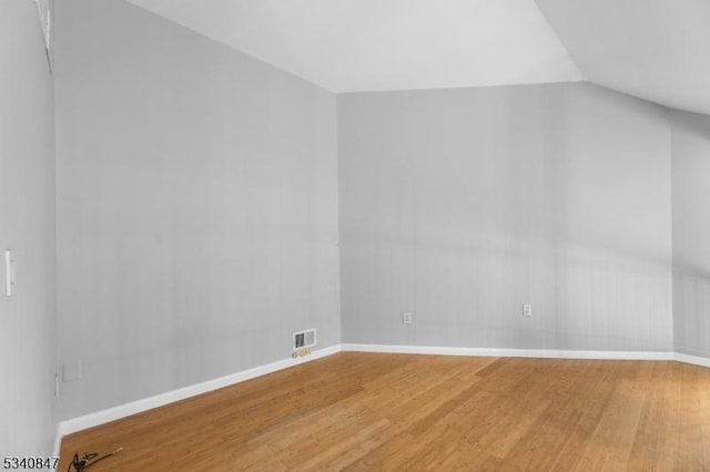 empty room featuring lofted ceiling, visible vents, baseboards, and wood finished floors