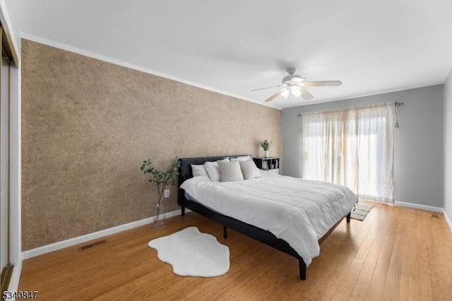 bedroom featuring visible vents, a ceiling fan, ornamental molding, wood finished floors, and baseboards