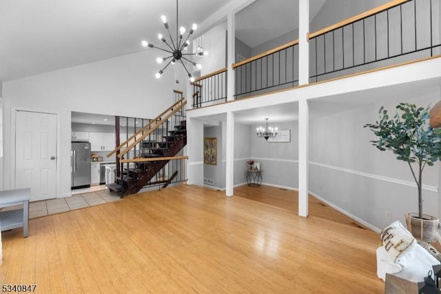 living area featuring high vaulted ceiling, light wood finished floors, stairway, and a notable chandelier