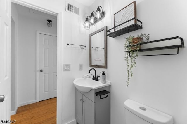 half bathroom with toilet, wood finished floors, vanity, visible vents, and baseboards