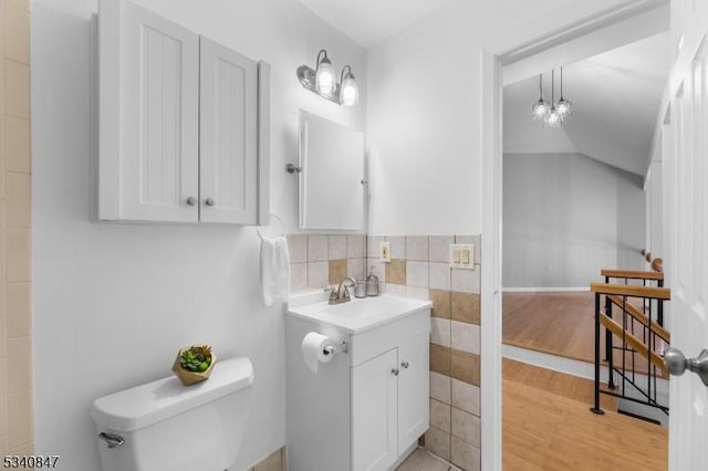 bathroom featuring lofted ceiling, toilet, wood finished floors, vanity, and tile walls