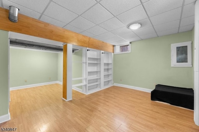 basement featuring a paneled ceiling, baseboards, and wood finished floors