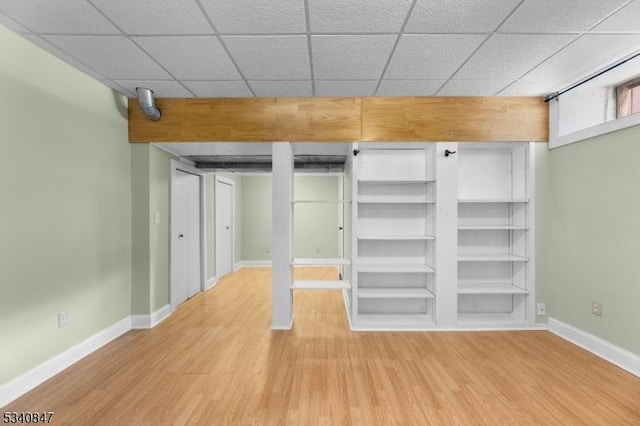 unfurnished bedroom featuring a drop ceiling, baseboards, and wood finished floors