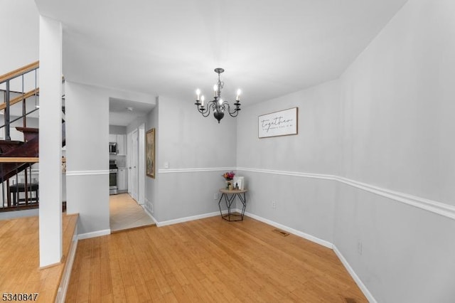 unfurnished dining area featuring a chandelier, stairway, wood finished floors, and baseboards