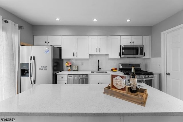 kitchen with light stone counters, decorative backsplash, appliances with stainless steel finishes, white cabinetry, and a sink