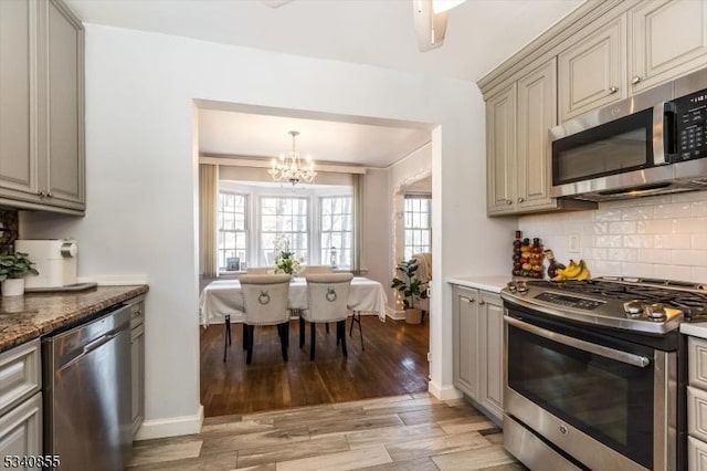 kitchen with backsplash, an inviting chandelier, appliances with stainless steel finishes, light wood-type flooring, and baseboards