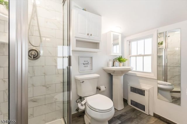 bathroom featuring a stall shower, wood finished floors, toilet, and radiator